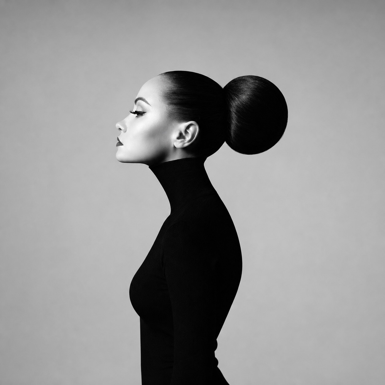 Black-and-white profile portrait of a woman with a sleek hair bun, in a black turtleneck